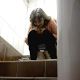 An older Eastern-European woman is recorded by a hidden camera as she takes a shit into a public floor toilet and wipes her ass. Background noise covers poop sounds. About a minute.